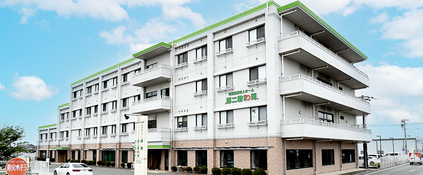 緑色の庭園ロゴが特徴的な白と煉瓦調の介護施設建物