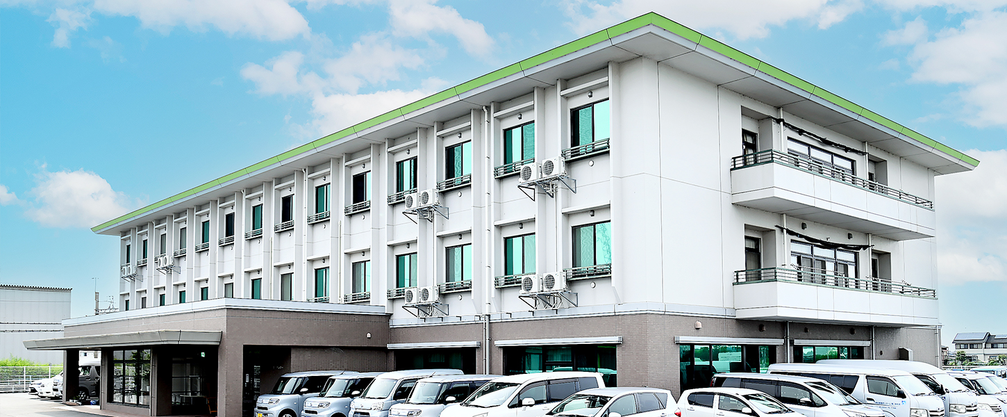 白とグリーンの近代的な介護施設の建物外観。駐車場完備。